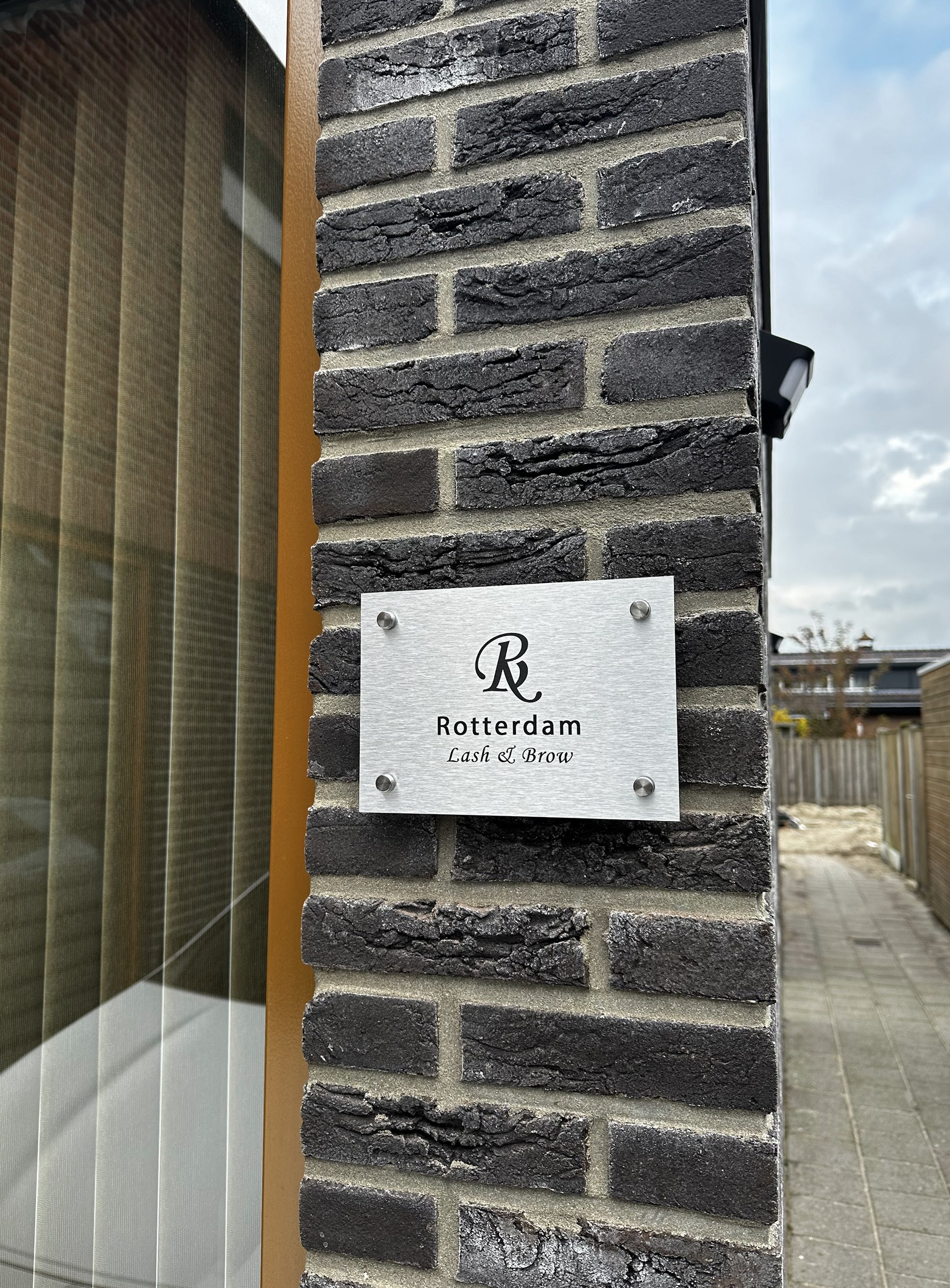 Het naambord van Rotterdam Lash & Brow op een donkere bakstenen muur bij de voordeur